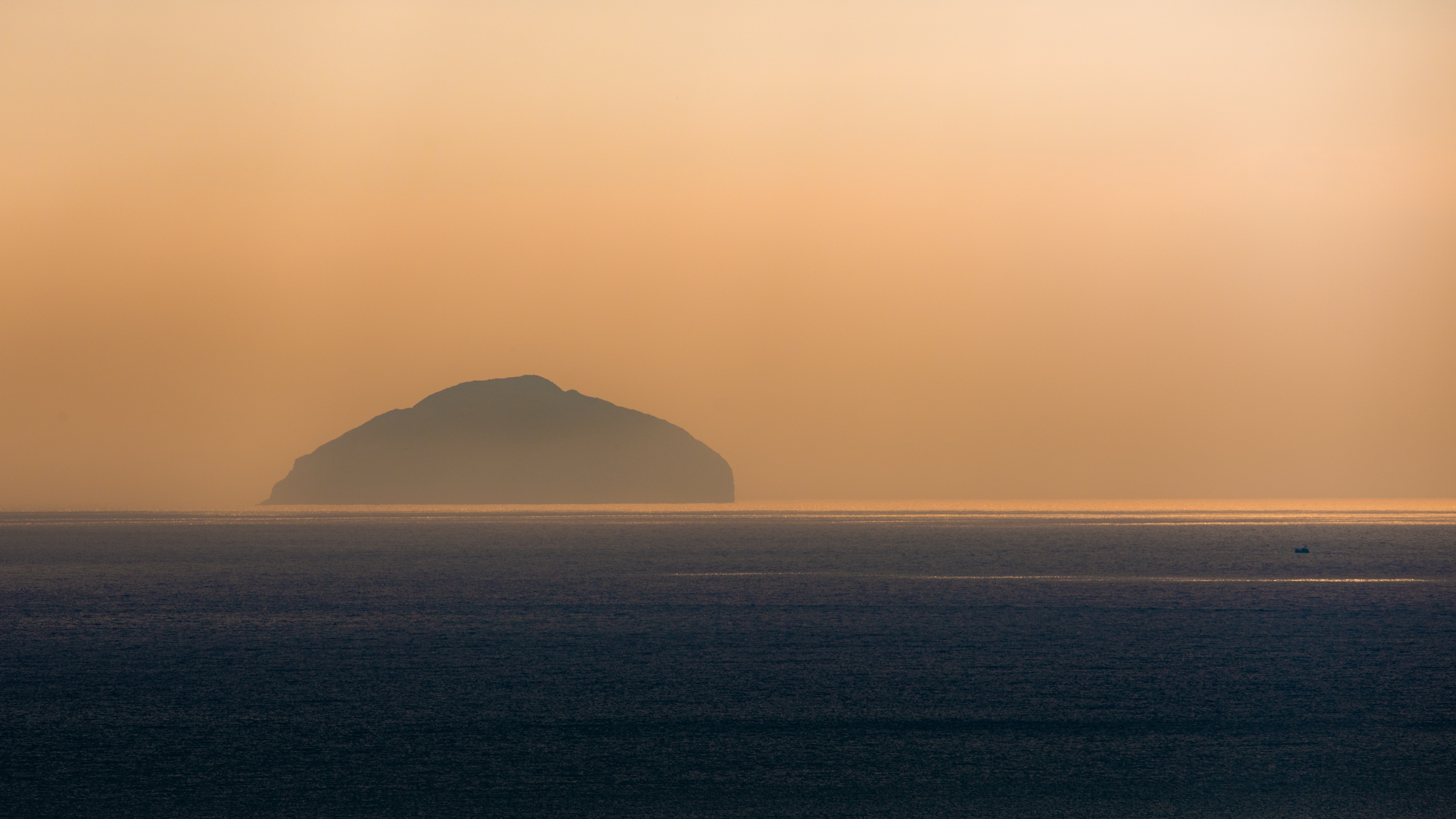 Minimal photo of an island in silhouette against a faded orange sky, dark sea in the foreground 